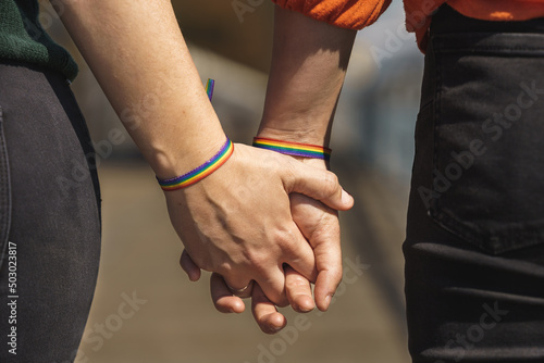 intertwined hands of lesbian couple with a rainbow bracelet