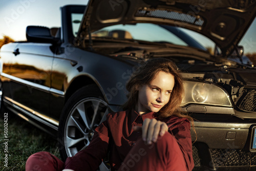 A beautiful girl near a car broken down in a field, a retro conv