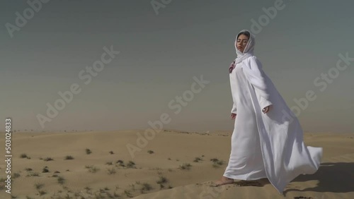 Arabic woman wearing abaya which is blowing on the wind in the desert photo