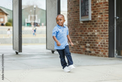 A cute little boy of preschool age with a blue shirt downtown in the city wearing denim jeans running around