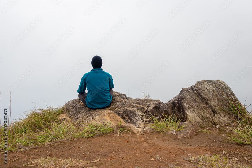man sitting alone at mountain rock with white mist background from flat angle