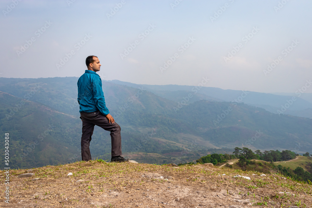 Naklejka premium man standing alone at hill top with misty mountain rage background from flat angle