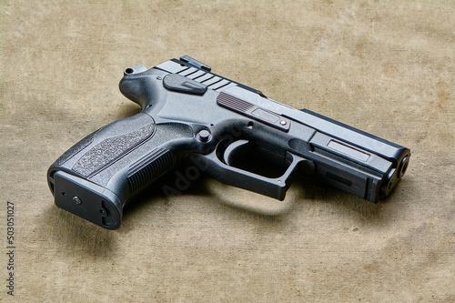 A black pistol in close-up lies on a canvas background, a firearm