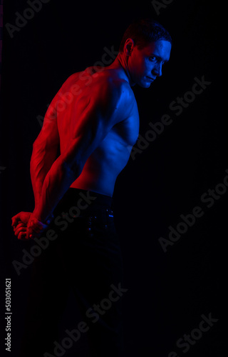 bare-chested man in colored light. shows muscles, poses with his back to us. Black background