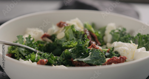 eat salad with kale, sundried tomatoes and mozzarella in white bowl closeup