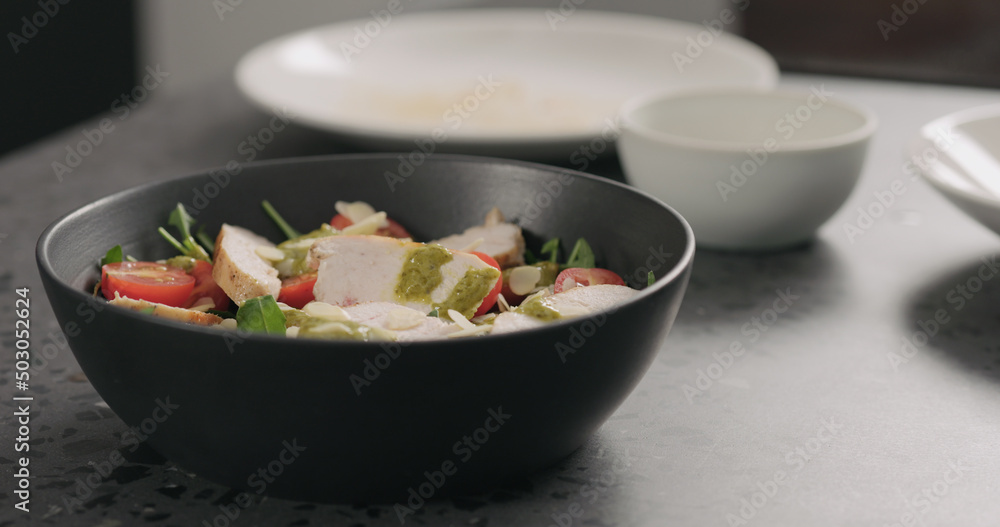almond flakes falling on salad with chicken, arugula and tomatoes in black bowl almond flakes falling on salad with chicken, arugula and tomatoes in black bowl