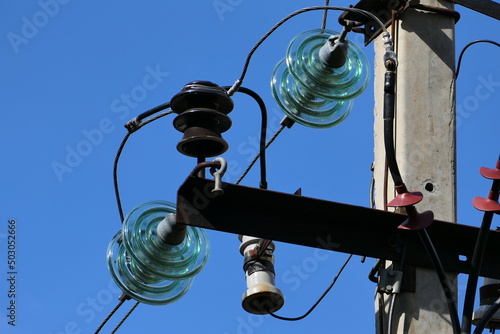 Close-up of high-voltage power lines and power pylons against a blue sky.