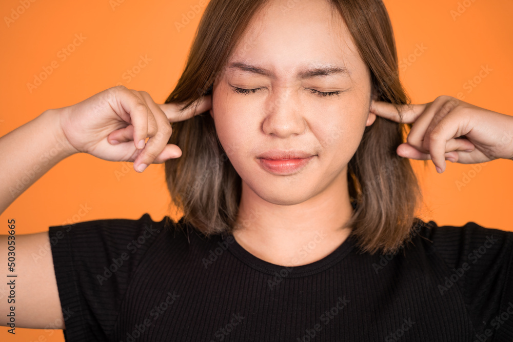 asian woman with annoyed expression covering ears with both hands on isolated background asian woman with annoyed expression covering ears with both hands on isolated background