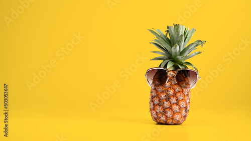 Pineapple with sunglasses against yellow background with copy space. Beach and tropical theme.