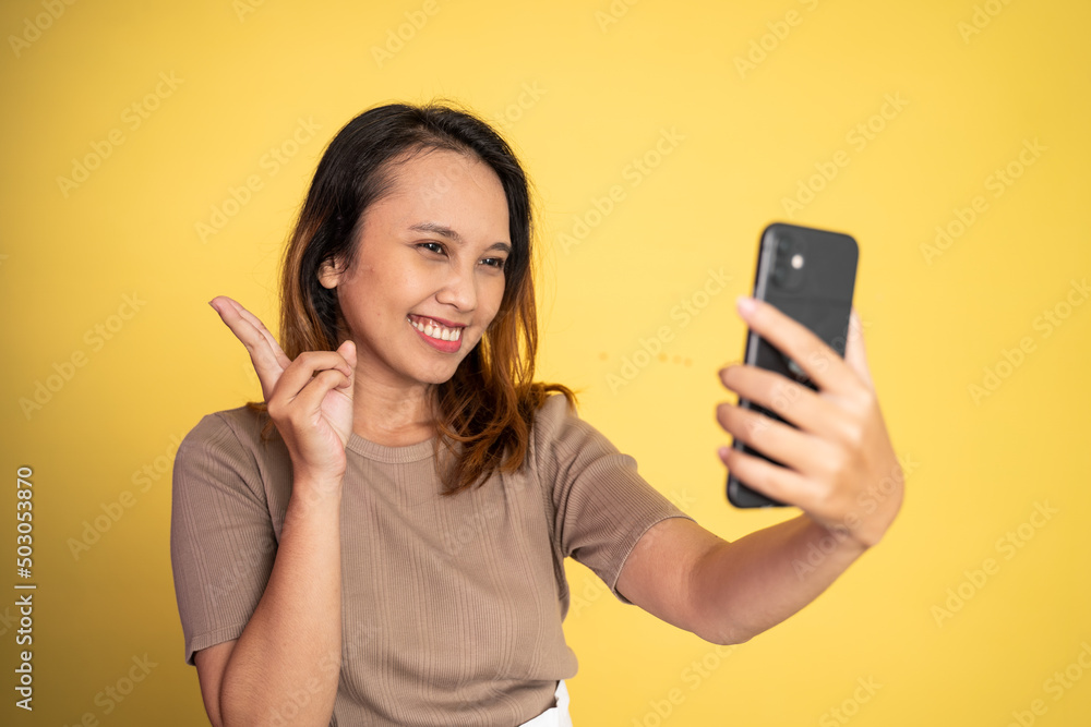 attractive woman take a selfie using mobile phone camera with v sign finger gesture on isolated background attractive woman take a selfie using mobile phone camera with v sign finger gesture on isolated background