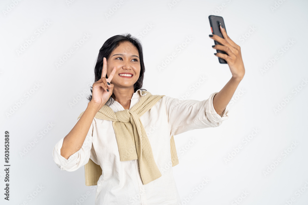 attractive woman take a selfie using mobile phone camera with v sign finger gesture on isolated background attractive woman take a selfie using mobile phone camera with v sign finger gesture on isolated background