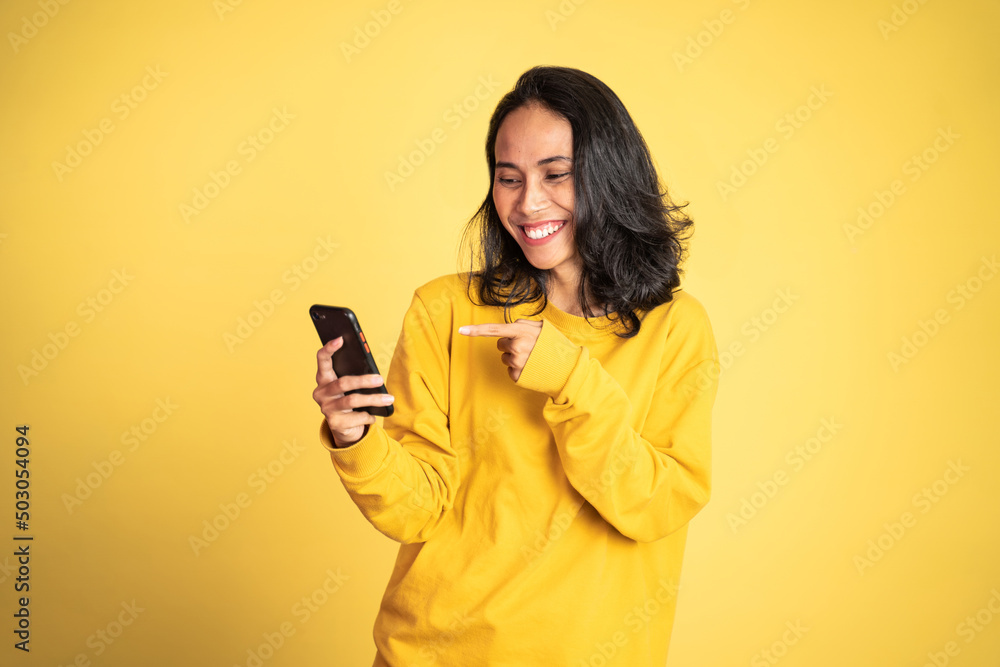 excited asian woman laugh with finger pointing on her mobile phone isolated background excited asian woman laugh with finger pointing on her mobile phone isolated background