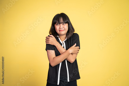 young woman feeling cold with both hands hugging her arms standing on isolated background © Odua Images