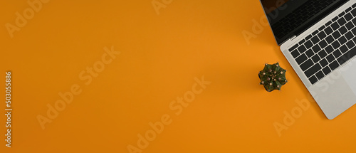 The top position view of a laptop computer next to a cactus with orange as the background ready for text or advertising. Flat lay composition.