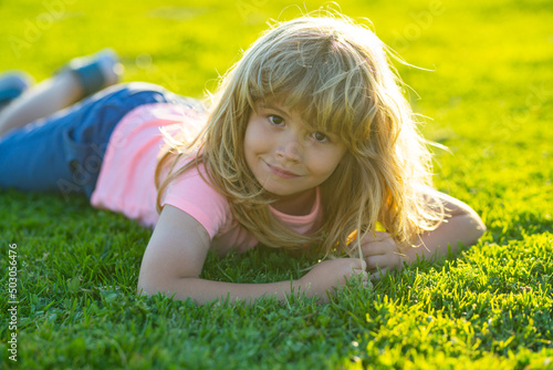 Spring child face. Smiling child boy with grass background. Happy little boy lying on the grass at the spring day. Portrait of a smiling child lying on green grass in park.