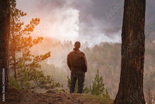a man looks at a burning fire in the forest. tourist or forest arsonist