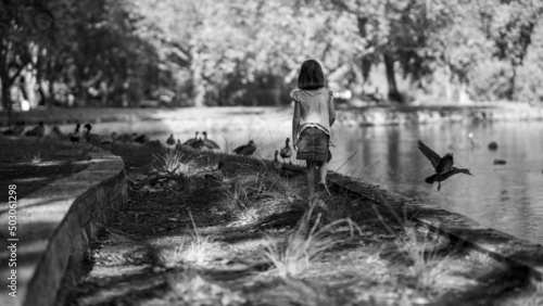 Grayscale shot of a girl walking on the lakeside with ducks in summer photo