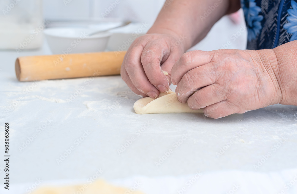 Senior woman hands making pies with apple filling on a white kitchen table with wooden rolling pin on background. Selective focus. Cooking at home concept. Tradition home-made food Senior woman hands making pies with apple filling on a white kitchen table with wooden rolling pin on background. Selective focus. Cooking at home concept. Tradition home-made food