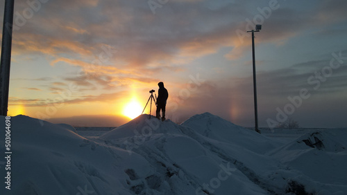 Photo Back view of a photographer with the camera on a tripod standing on a snowy hill