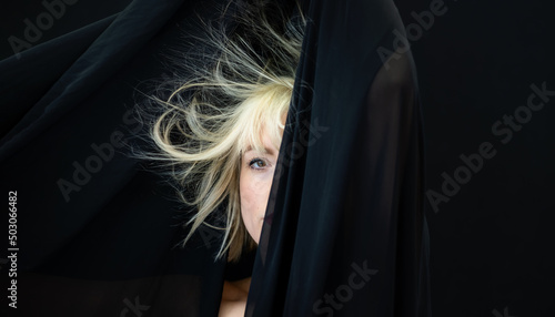 half hidden portrait of blonde sexy woman fashion model, behind black cloth, whose hair is electrostatic charged and hanging on the cloth