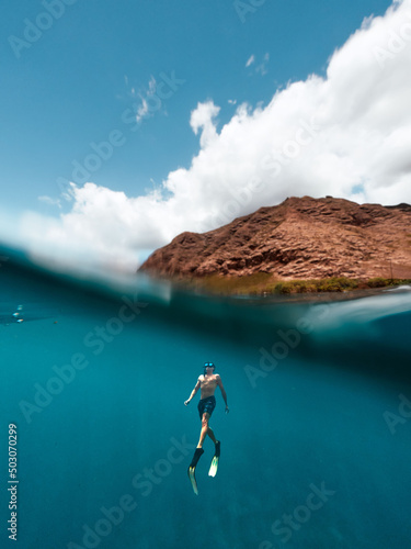 Mesmerizing shot of a male free diver swimming up to surface near to an island in bright sunlight photo