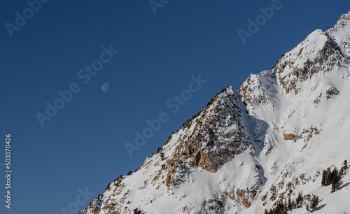 Beautiful view of the Moon setting over the Wasatch Mountains on a sunny day in Utah, United States photo