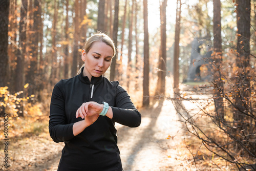 Active girl with fitness tracker smart watch running in the autumn park outdoors, viewing health data while doing sports by touching the screen of her smart watch