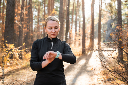 Active girl with fitness tracker smart watch running in the autumn park outdoors, viewing health data while doing sports by touching the screen of her smart watch