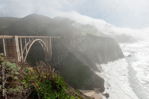 Bixby Canyon Bridge during a beautiful sunny afternoon, while a thin fog is creeping up from the sea. photo