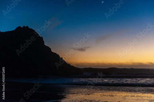 Bright orange sky at Pfeiffer beach  around sunset. Small crescent moon is in the background.