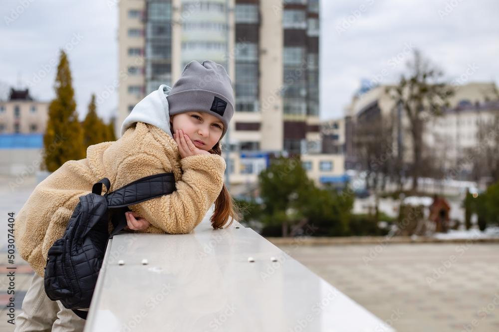 a cute seven-year-old girl in a faux fur coat stands near the parapet in the city