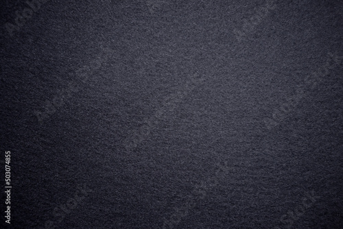 Photo of a black color texture. Black background for the text made of soft felt fabric. Dark textured background with vignette around the edges.
