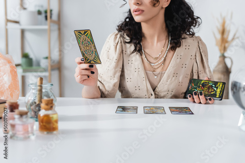 Fotografie KYIV, UKRAINE - FEBRUARY 23, 2022: Cropped view of fortune teller holding tarot cards near crystal at home
