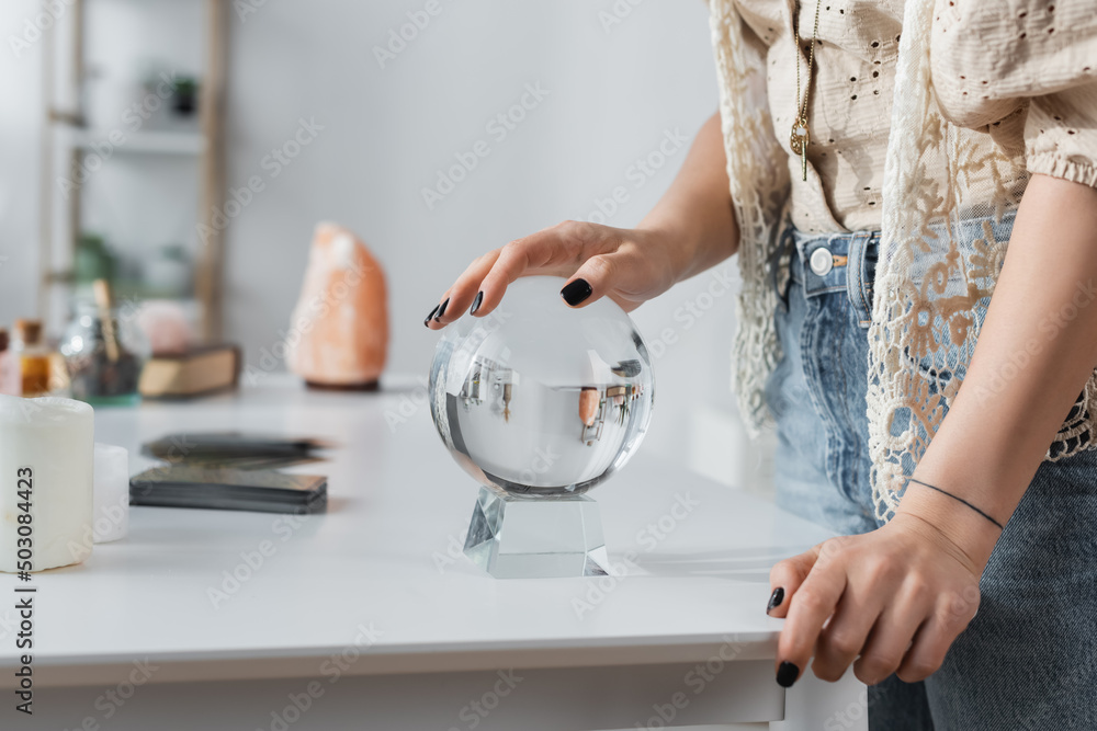 Cropped view of soothsayer touching orb near candles on table.