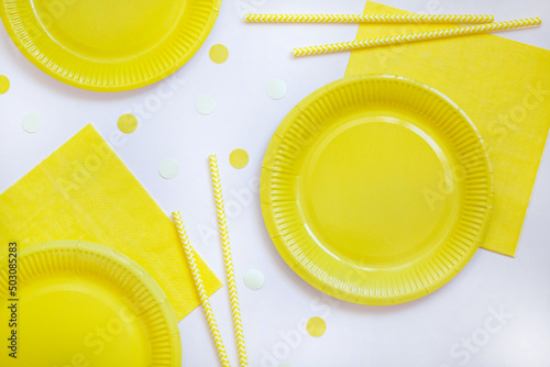 Yellow paper disposable plates, napkins and straws for drinks on white background. Table setting for picnic. Bright eco-court. Birthday, party and holiday concept. Top view, flat lay.