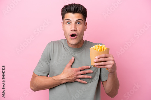 Young caucasian man holding fried chips isolated on pink background surprised and shocked while looking right