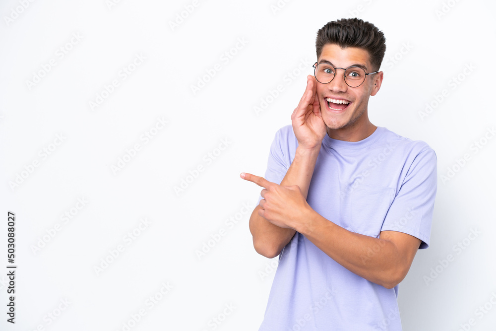 Young caucasian man isolated on white background pointing to the side to present a product and whispering something Young caucasian man isolated on white background pointing to the side to present a product and whispering something