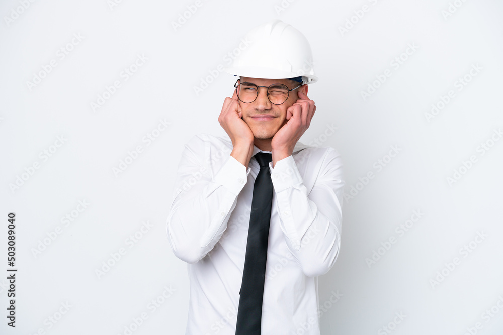 Young architect caucasian man with helmet and holding blueprints isolated on white background frustrated and covering ears