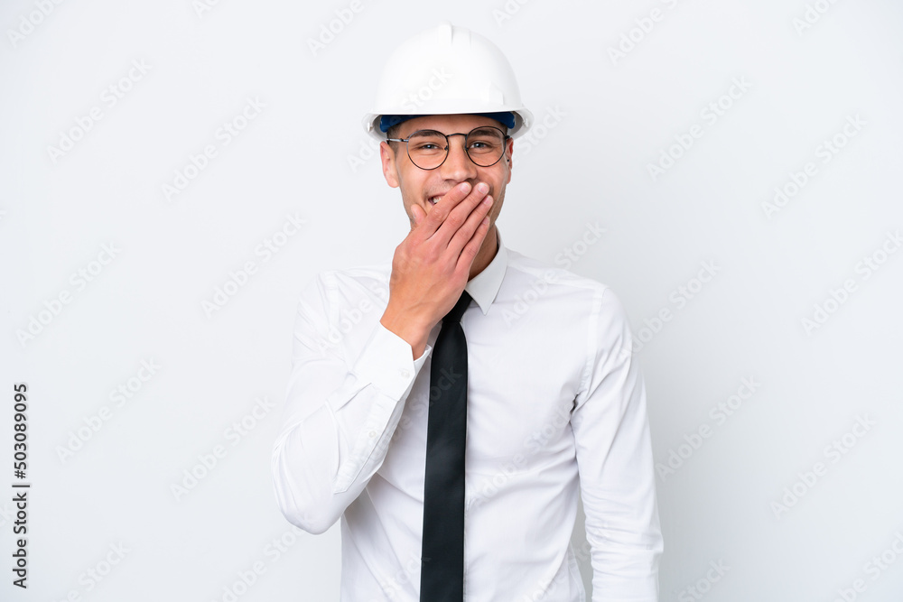 Young architect caucasian man with helmet and holding blueprints isolated on white background happy and smiling covering mouth with hand Young architect caucasian man with helmet and holding blueprints isolated on white background happy and smiling covering mouth with hand