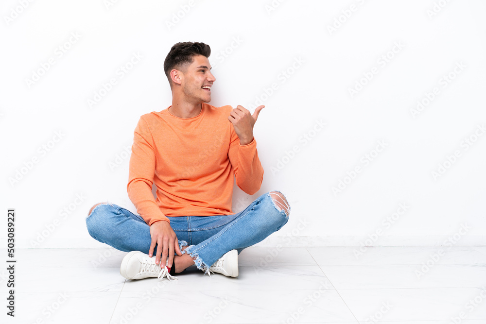 Young man sitting on the floor isolated on white background pointing to the side to present a product Young man sitting on the floor isolated on white background pointing to the side to present a product