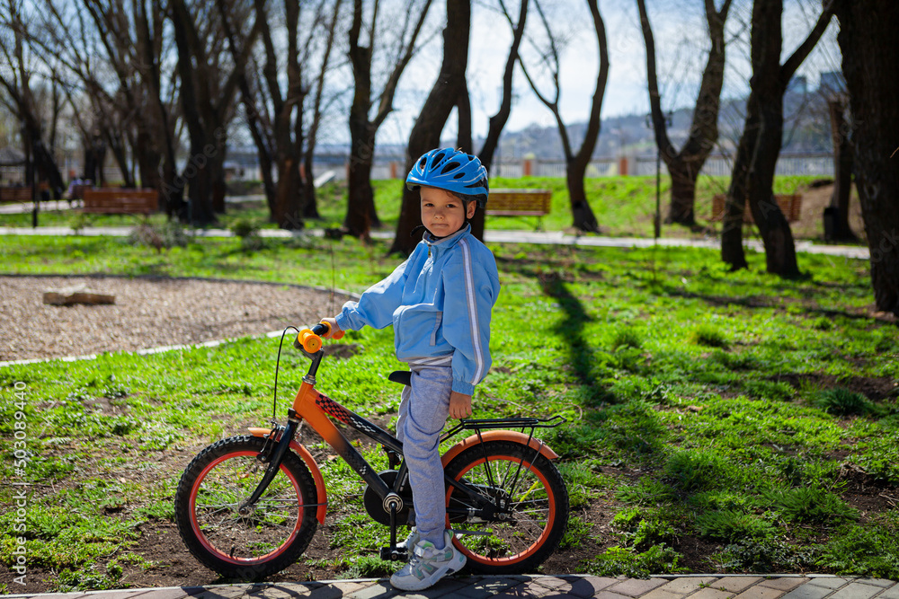 Fototapeta premium Happy kid boy of 5 years having fun in spring park with a bicycle on beautiful fall day. 