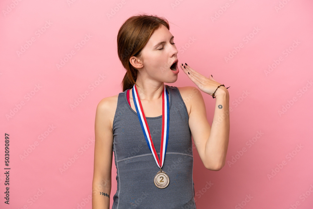 Young English woman with medals isolated on pink background yawning and covering wide open mouth with hand Young English woman with medals isolated on pink background yawning and covering wide open mouth with hand