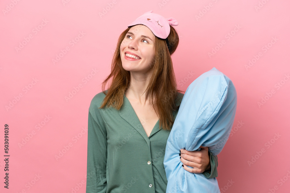 Young English woman in pajamas isolated on pink background in pajamas and looking up while smiling Young English woman in pajamas isolated on pink background in pajamas and looking up while smiling