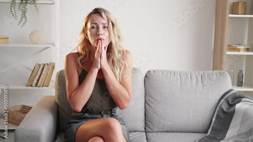 Negative news. Shocked woman. Unexpected situation. Confused casual lady feeling disbelief emotion sitting sofa in light room interior copy space. photo