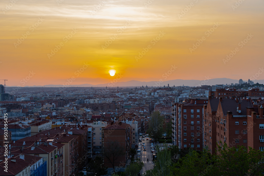 Obraz premium An amazing warm sunset over the skyline of Madrid with views on the mountain range, Sierra de Guadarrama on the horizon, seen from las siete tetas on Cerro Tio Pio hill side.