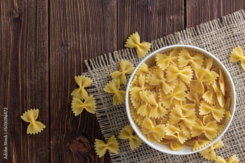 Raw pasta farfalle in bowl on sackcloth with copy space on wooden background.