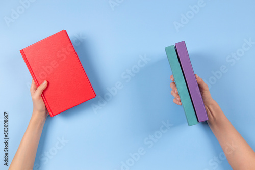 Hands holding books over light blue background. Education, self-learning, book swap, sharing, bookcrossing concept