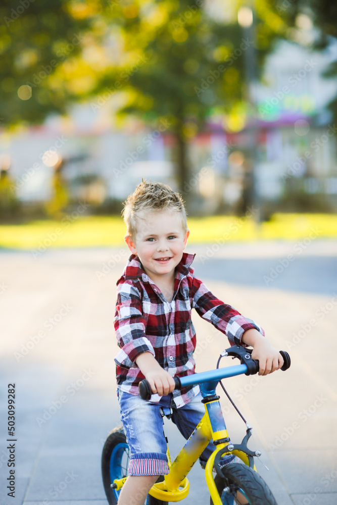 stylish European boy in shirt and jeans rides balance bike on asphalt. Child riding without helmet stylish European boy in shirt and jeans rides balance bike on asphalt. Child riding without helmet