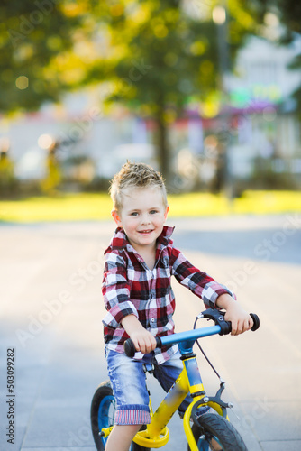 stylish European boy in shirt and jeans rides balance bike on asphalt. Child riding without helmet
