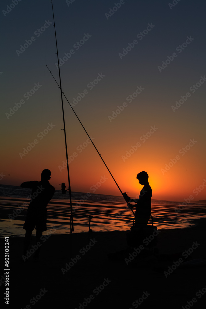 silhouette of two fishermen on a beach at sunset